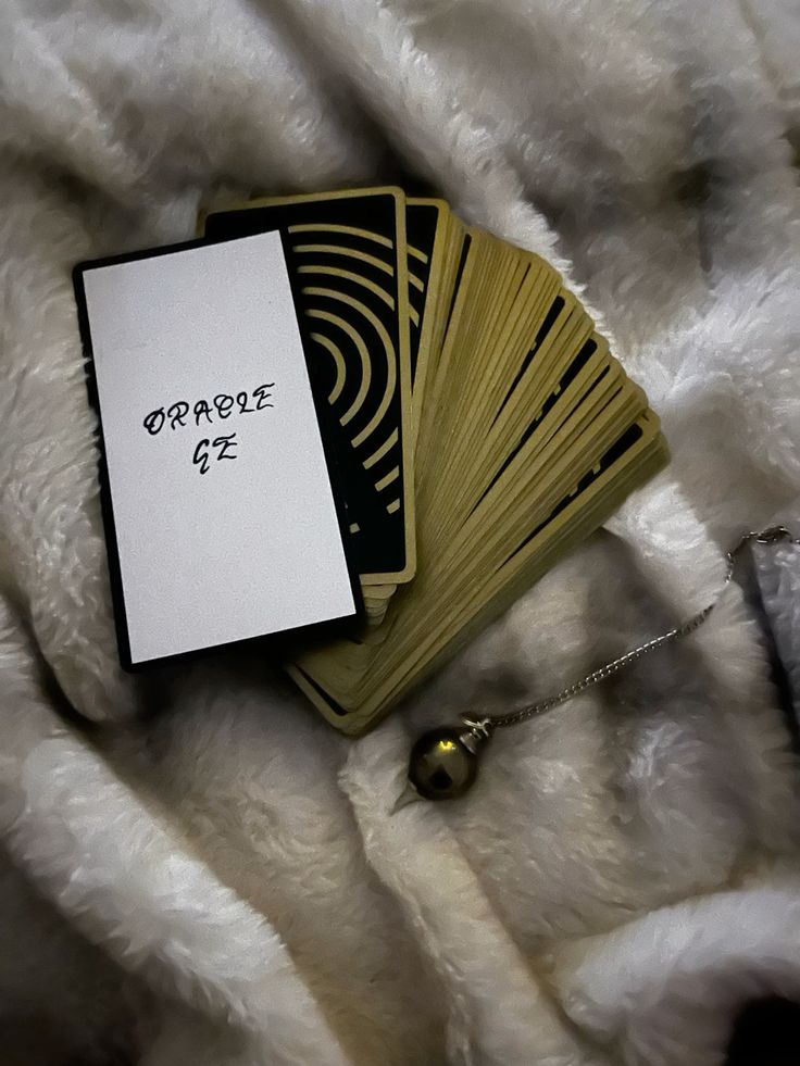 Le jeu d'oracle de Sam, déployé en éventail : dos noirs ornés d'arcs dorés, posés sur une étoffe claire, à côté d'un pendule.